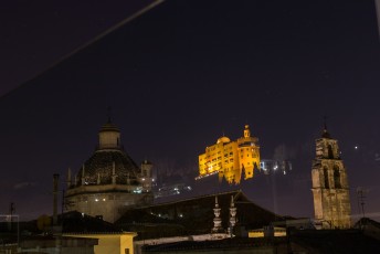 's Avonds reflecteerden de sterren en het hotel Alhambra Palace in het glas van het balkon terwijl de kerk aan de overkant erdoorheen zichtbaar is.